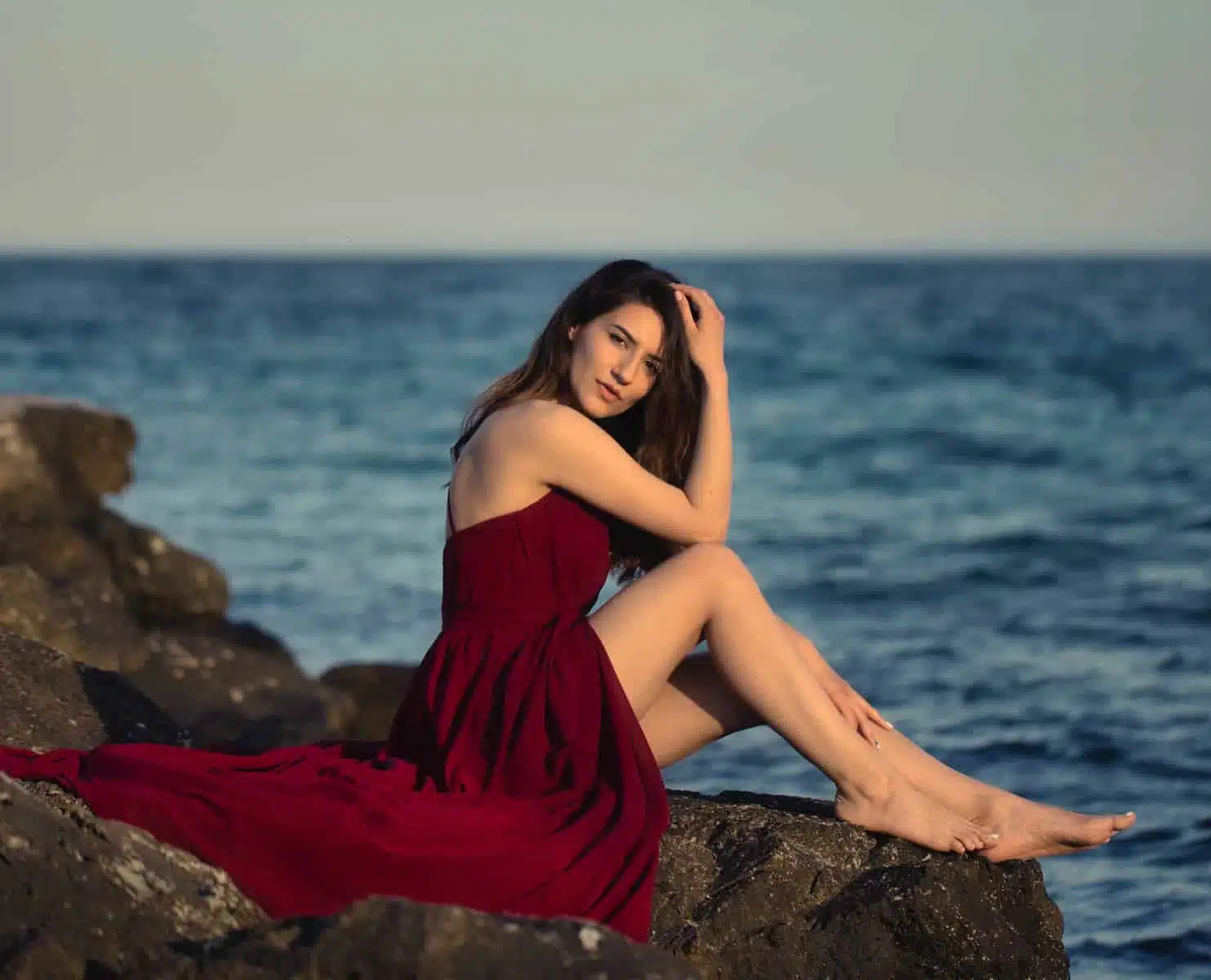 woman in red dress sitting on rock near sea during daytime